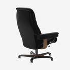 A black leather ergonomic office chair with a high back, padded armrests, and a wooden accent panel near the footrest, shown on a light gray background.