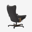A black leather ergonomic office chair with a high back, padded armrests, and a wood-grain accent panel on the side, shown from a three-quarters angle on a light gray background.